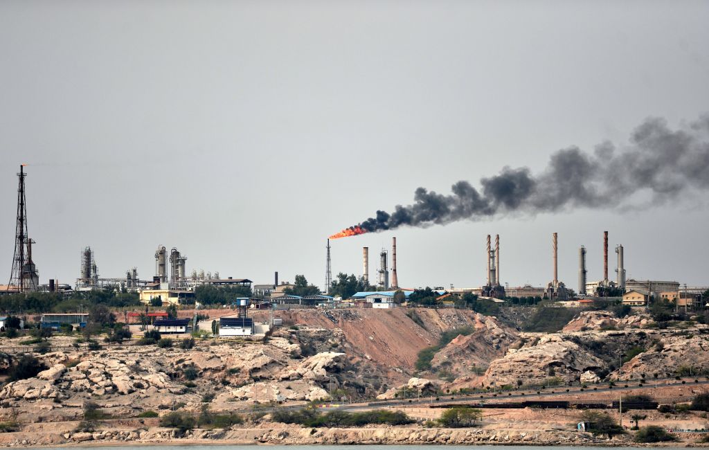 Flare stack burning at an oil refinery with a large smoke plume, illustrating energy market volatility.