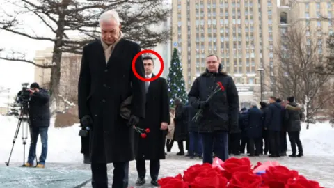 Evgeny Lyukshin (circled) standing behind Russian Deputy Foreign Minister Alexander Grushko at a memorial event