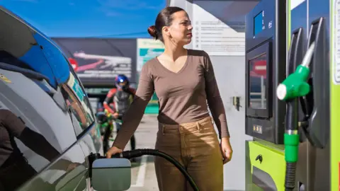 A woman pumps petrol into her car, illustrating fuel costs for consumers.