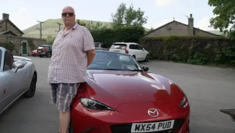 Red Mazda MX-5 convertible with its owner standing beside it
