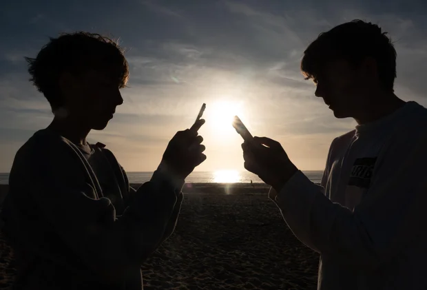 Two teenage boys look at smartphones at sunset in Cornwall, England, June 1, 2026.